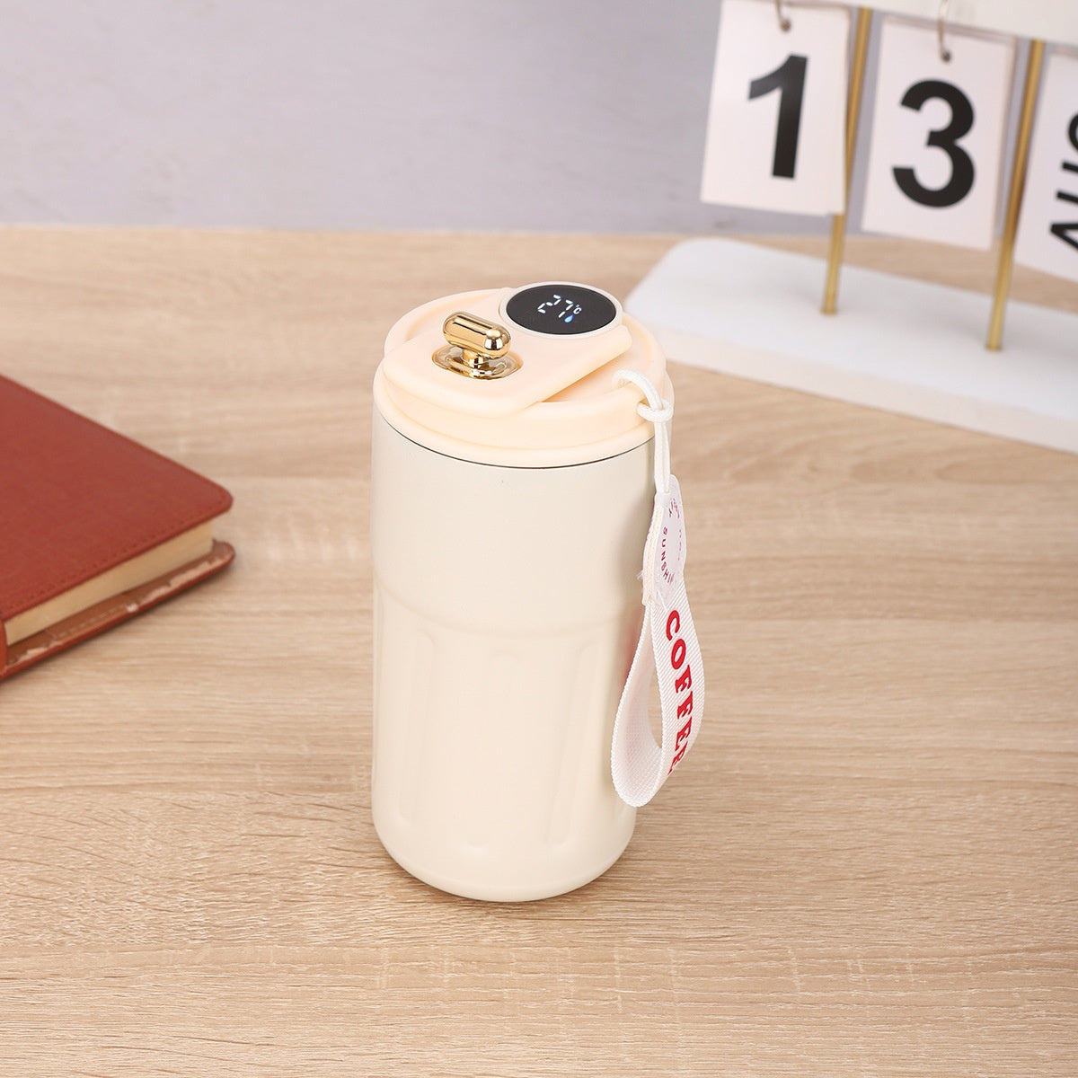 White ceramic mug with gold lid on a wooden surface, featuring a «Coffee» tag.