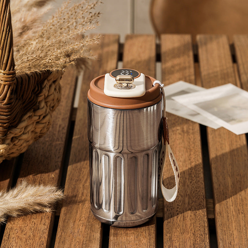 Silver tumbler with coffee lid on a wooden surface.