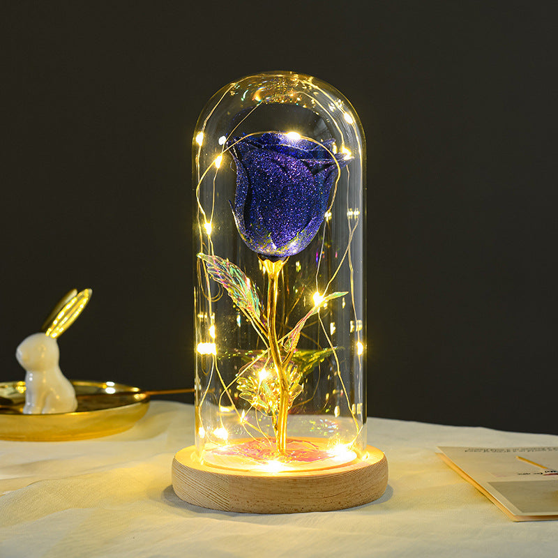 Blue rose in a glass dome with LED lights on a wooden base against a dark background