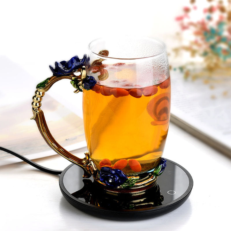 Glass mug with floral handle filled with a hot beverage on a black coaster.