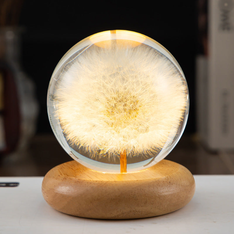 Decorative lamp with a dandelion seed head inside a glass sphere on a wooden base.
