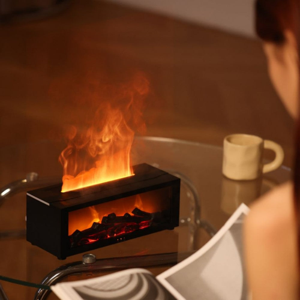 Small electric fireplace with flames on a glass table, person holding a book in the foreground.