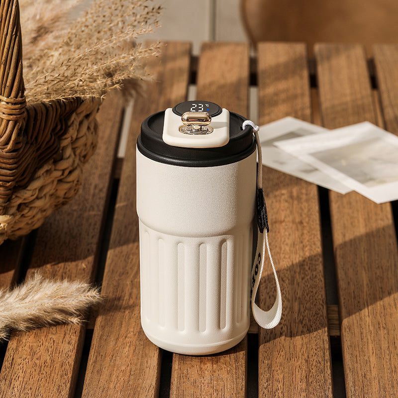 White insulated coffee cup with black lid on a wooden surface.