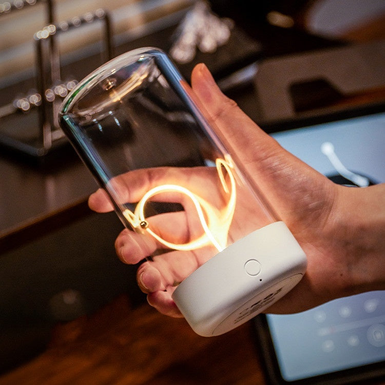 Hand holding a portable led night light with glowing interior, connected to a white device, in a kitchen setting.