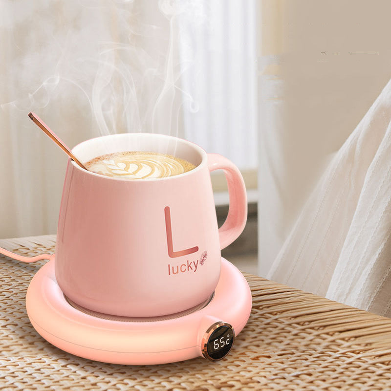 Pink mug with «Lucky» on a heating pad, containing a hot beverage.