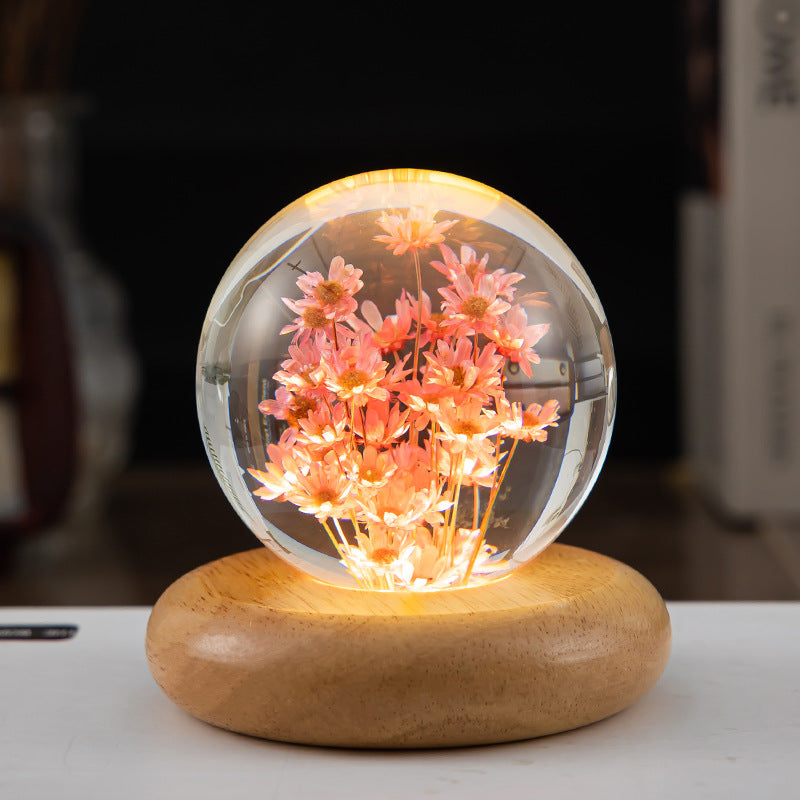 Clear glass sphere with pink flowers and LED lights on a wooden base