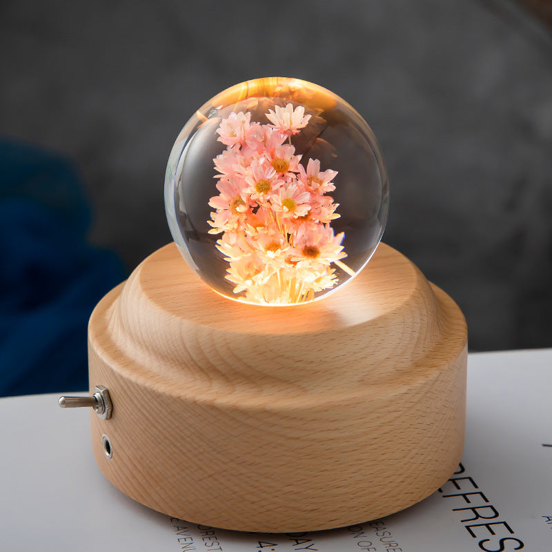 Decorative lamp with a glass sphere containing flowers on a wooden base.
