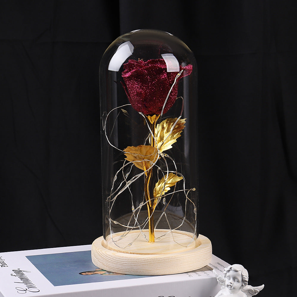 Red rose with gold leaves under a glass dome on a black background.