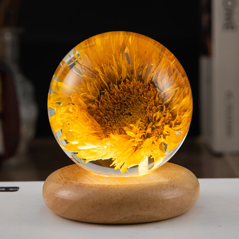 Glass sphere with a sunflower inside on a wooden base, against a blurred background.