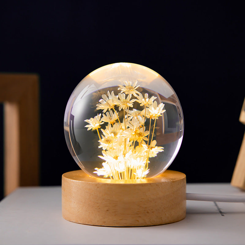 Decorative lamp with glass sphere containing illuminated flowers on a wooden base.