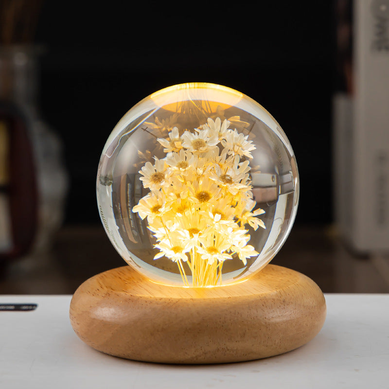 Decorative lamp with glass sphere containing flowers on a wooden base.