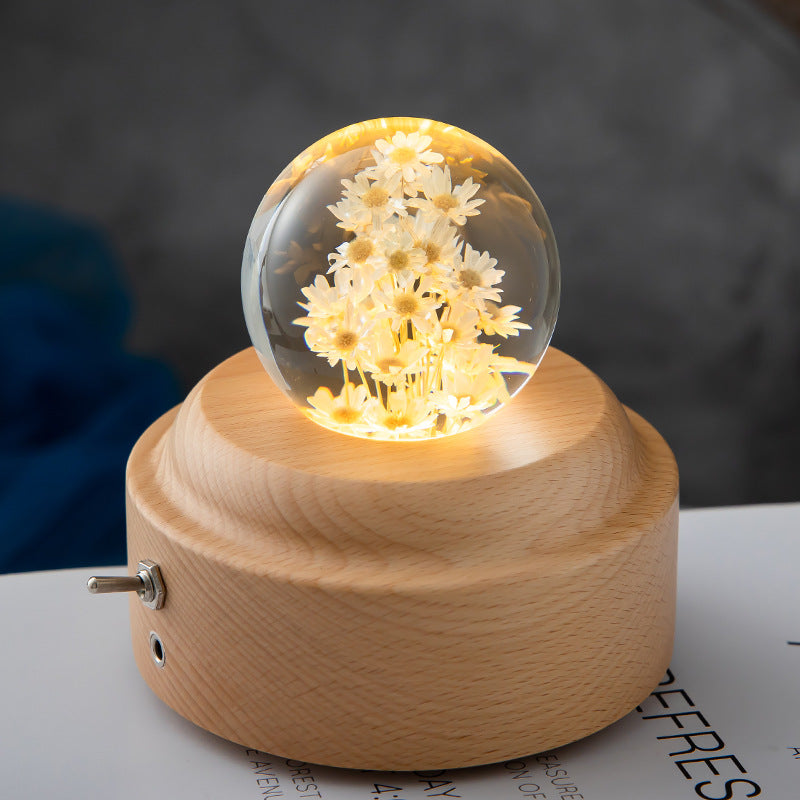 Decorative lamp with a glass sphere containing flowers on a wooden base.
